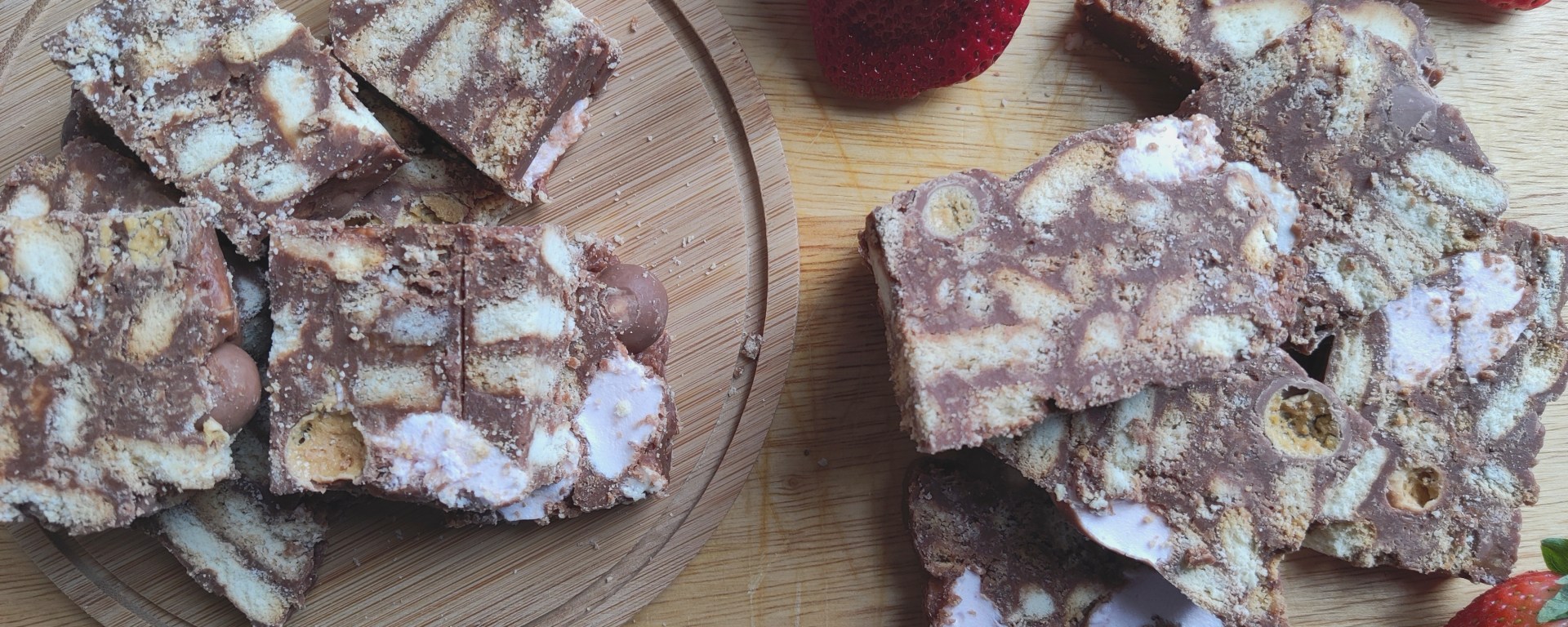 Slices of Rocky Road with fresh strawberries on a chopping board.