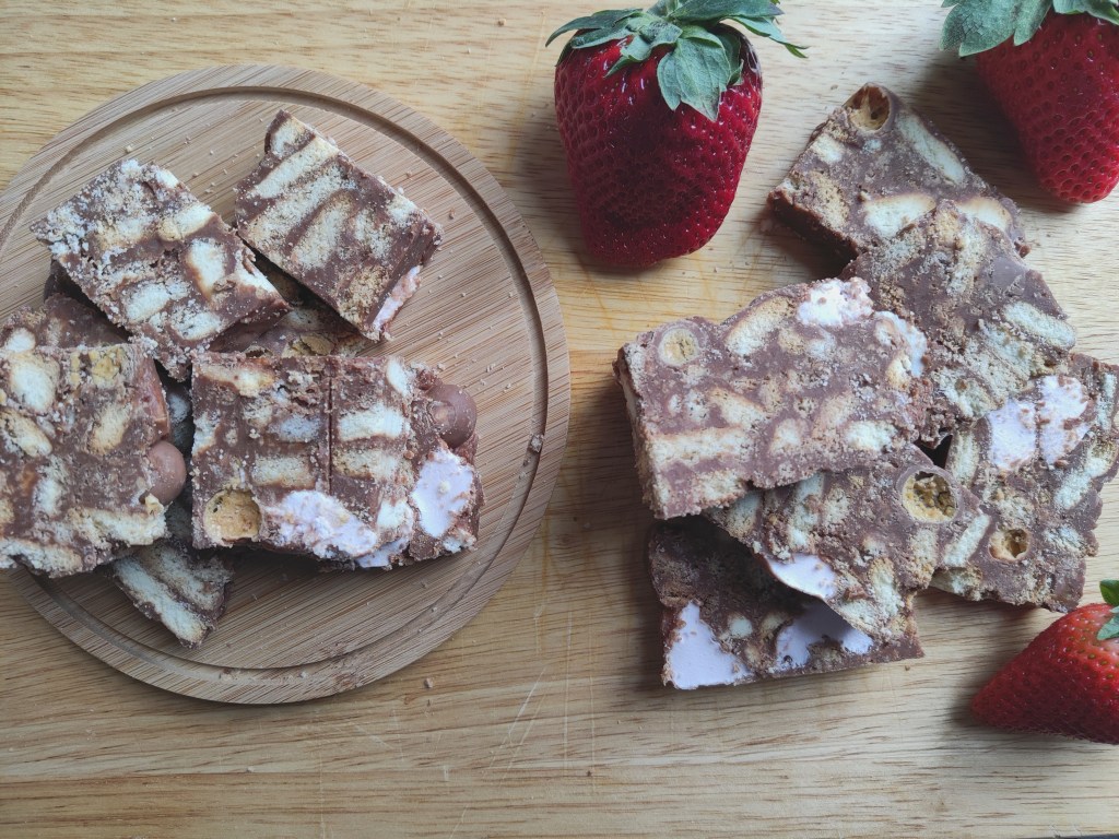 Slices of Rocky Road with fresh strawberries on a chopping board.