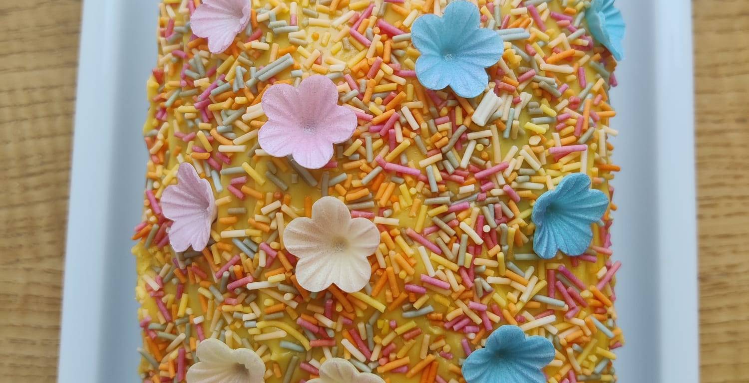 Loaf cake withe yellow buttercream icing, coloured sprinkles and coloured wafer flowers.